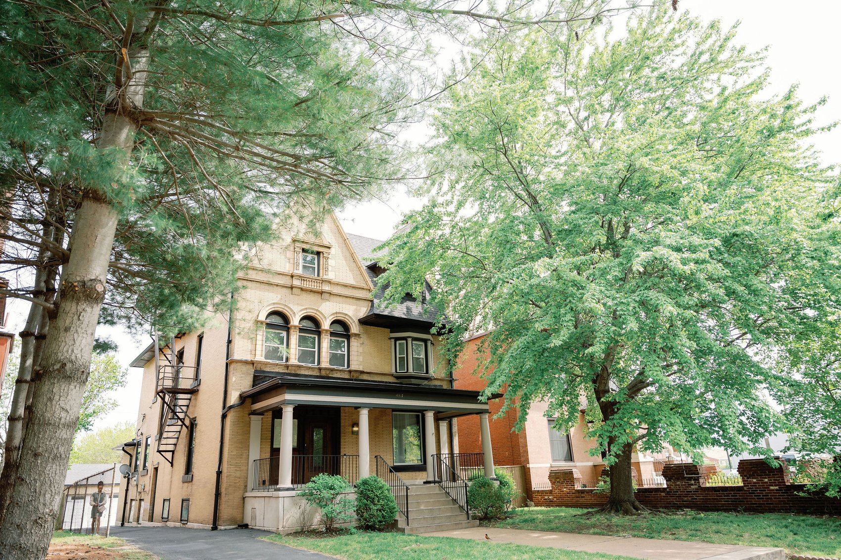 The exterior of Korédé House, a yellow-brick Victorian framed by trees