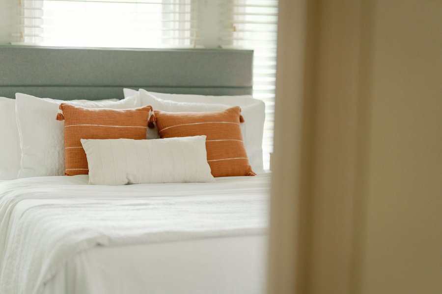 A made bed at Korédé House with white linens and rust cushions